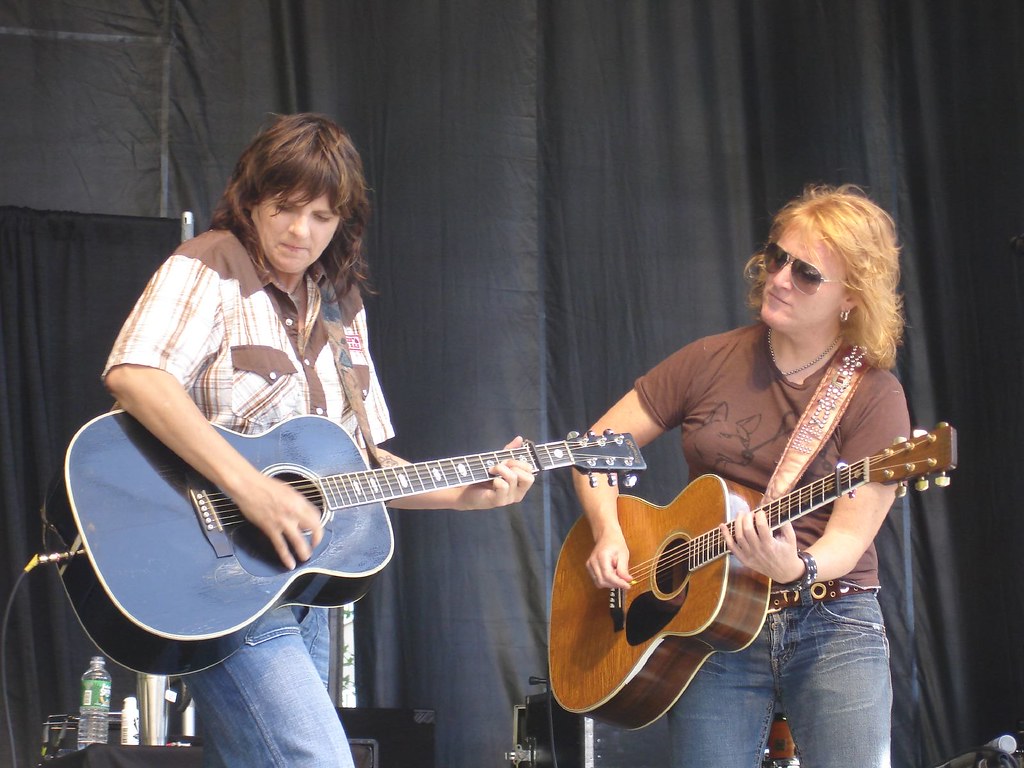 Two women in casual clothing play guitar on a stage