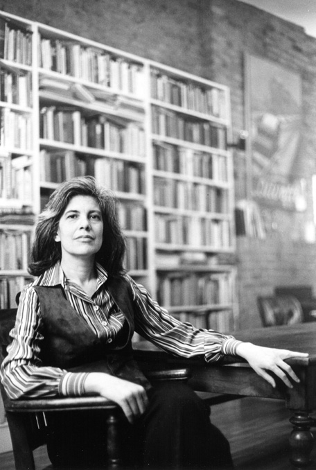 A black and white photo of Susan Sontag in front of a bookshelf