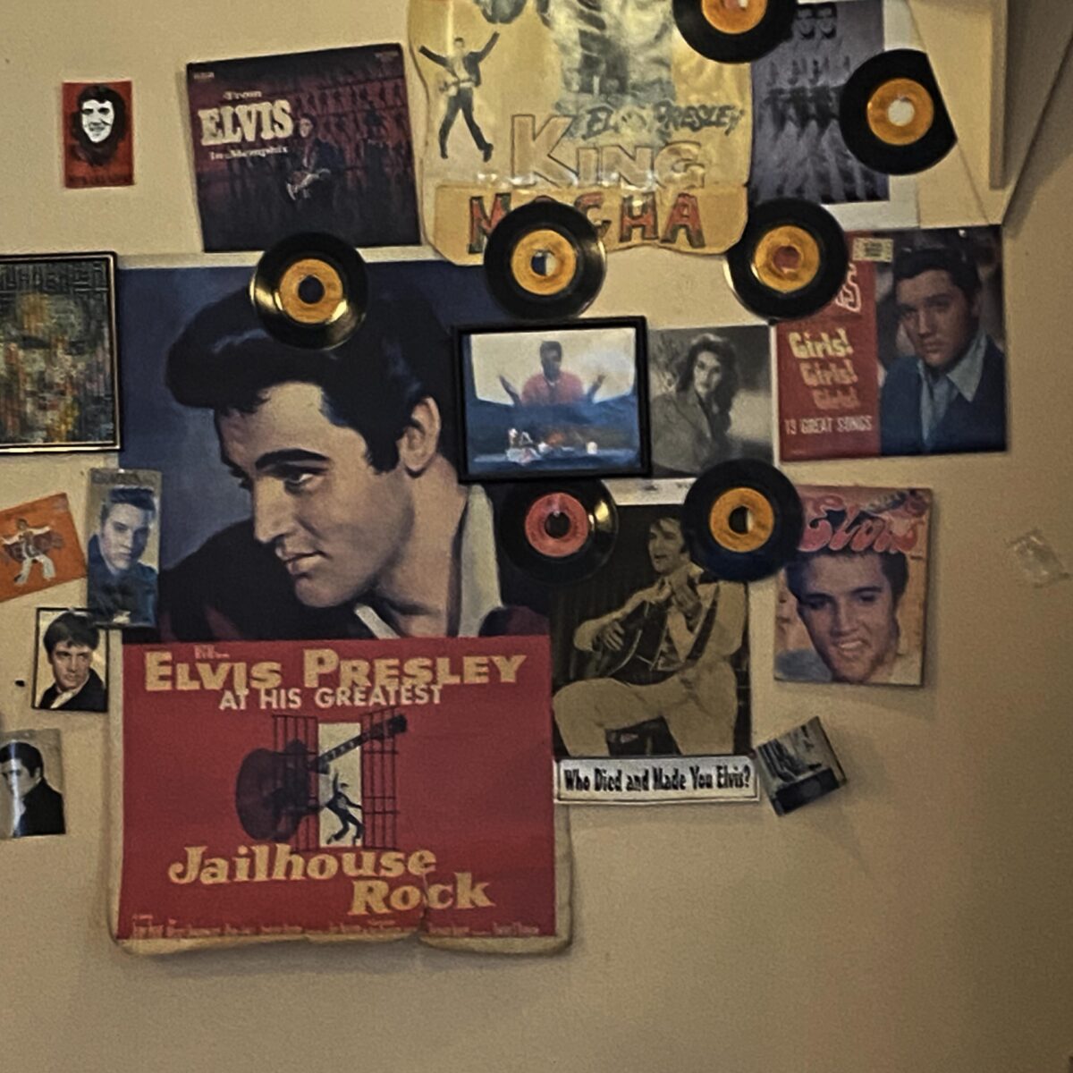 This photograph features a light brown wall at coffeeshop Cup A Joe in Raleigh, NC. The wall is covered with pictures of Elvis Presley and small orange and red vinyls.