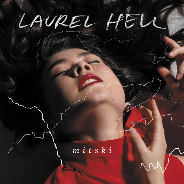 Mitski's album cover for "Laurel Hell." It is a picture of her craning her neck backwards and holding her hands out. She is wearing a red turtleneck.White text reads "Laurel Hell" and "Mitski"