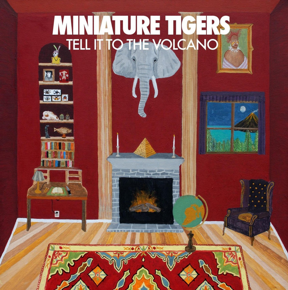 Miniature Tigers' album cover for "Tell It to the Volcano." A red painted room with wood floors and an elephant head hung above a fireplace. White text at the top-center of the photo that reads "Miniature Tigers Tell it to the Volcano"
