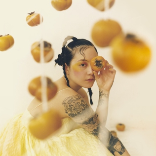 Michelle Zauner posed amongst yellow persimmons. Japanese Breakfast's album cover for "Jubilee."