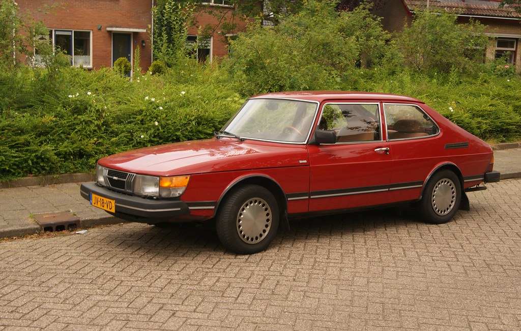 Red 1983 SAAB 900 GL on a street with shrubbery behind it. 