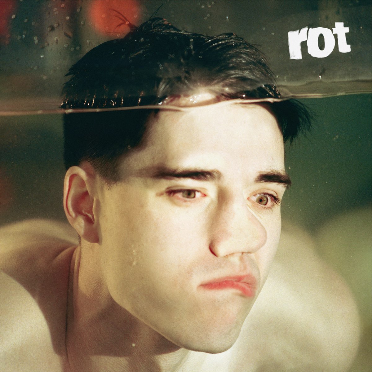 Album cover for "Rot" by Tennyson. Man underwater, the top of his head peaking out. He is pressing his face against the glass, smushing his nose and lip.