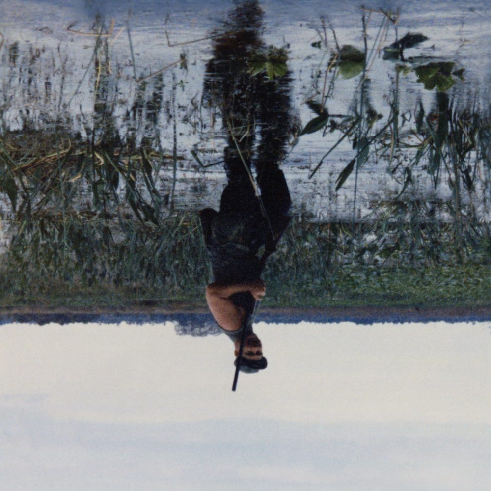 Cover for Animal Drowning by Knifeplay. Image of a person standing in a bog holding a shotgun. The image is upside down.
