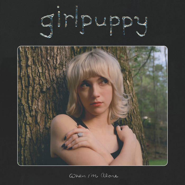 Girlpuppy's album art for "When I'm Alone." Image of a person standing in front of a tree hugging themself.