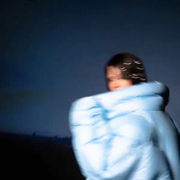 Cover art for Nymph by Shygirl. A person in a big blue puffer jacket standing against the sky.