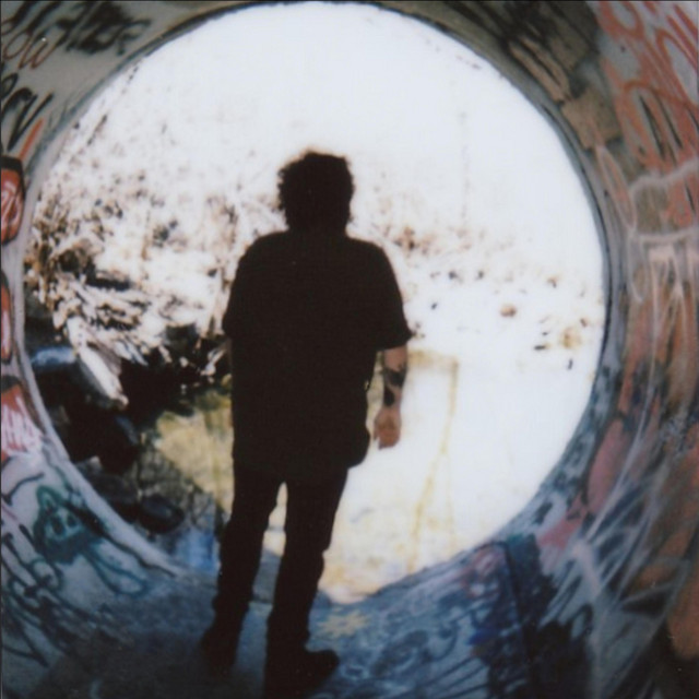 This image is the album cover of "sharp objects" by mark drizzle that shows the back silhouette of Mark as they stand in a tunnel covered with graffiti.
