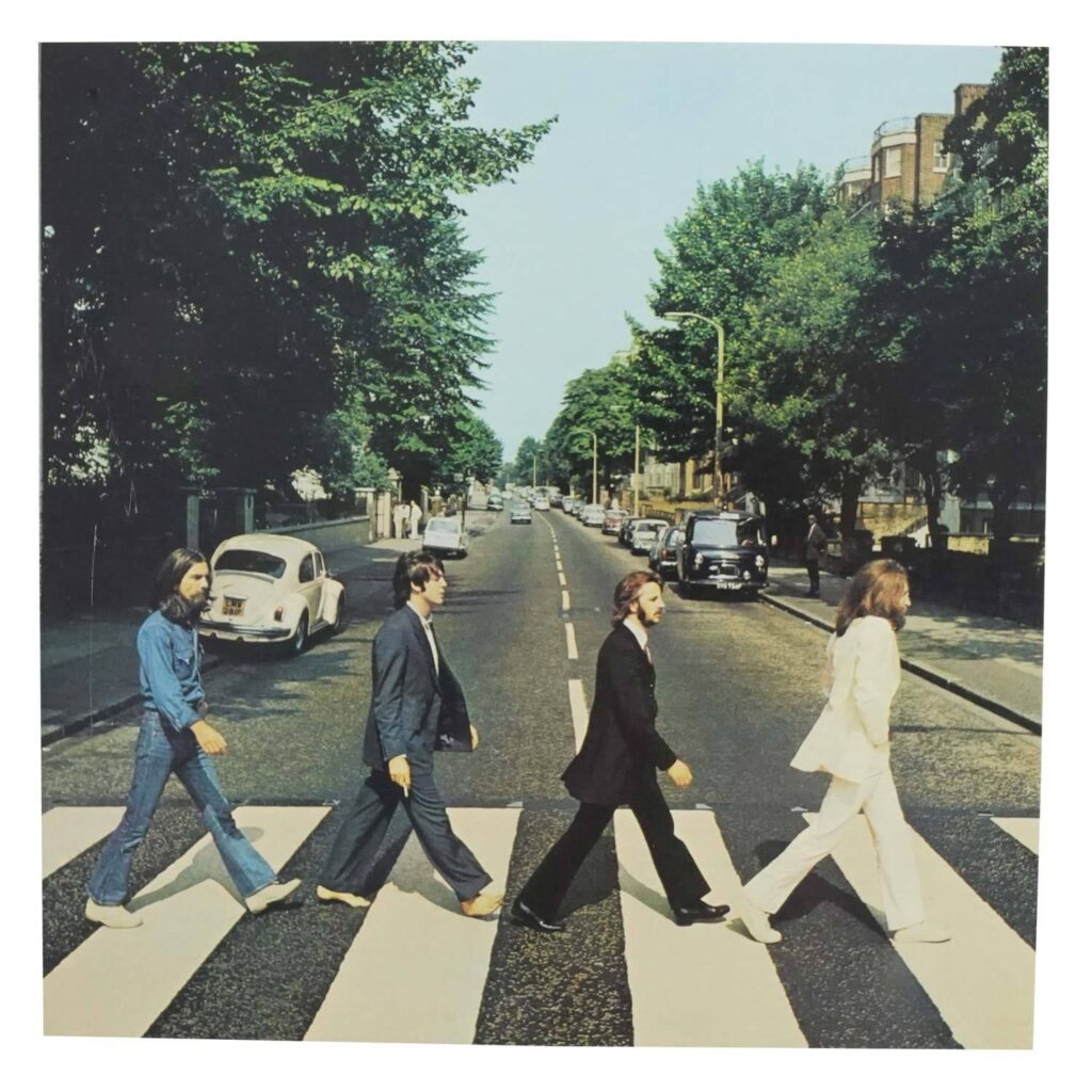 Album cover for "Abby Road" by the Beatles. It features the members of The Beatles walking through a sidewalk with a street in the background. 