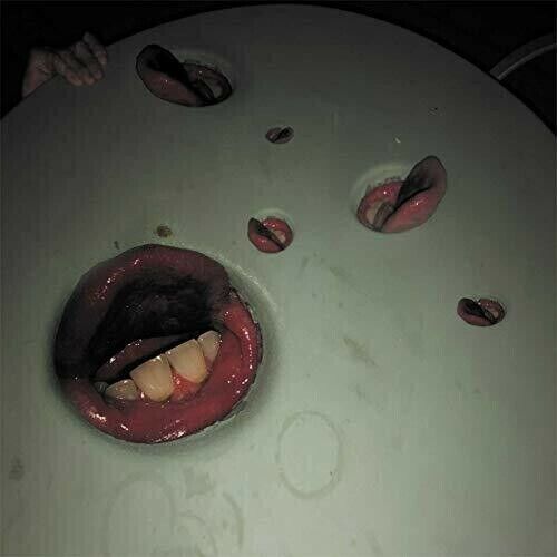 The album cover of "Year of the Snitch" by Death Grips. It features a grimy surface with holes in it. Each hole is filled by a mouth with tongues sticking out. A hand is gripping the side of the table. 