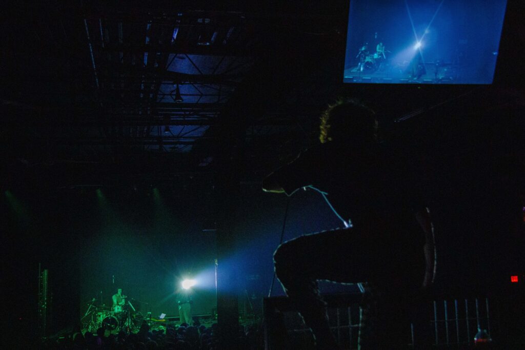 Silhouette of Matt Stephenson of Machine Girl standing above the crowd on a raised level at The Ritz. 