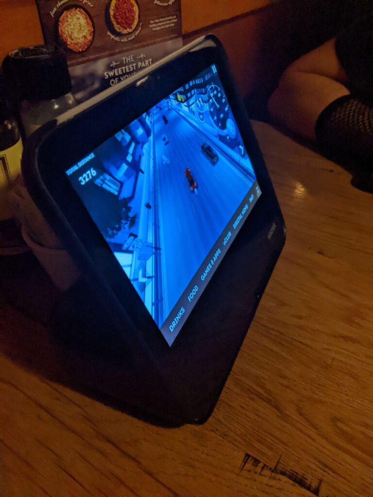 A tablet with a preview video of a very basic racing game, with options for the menu and games at the bottom.