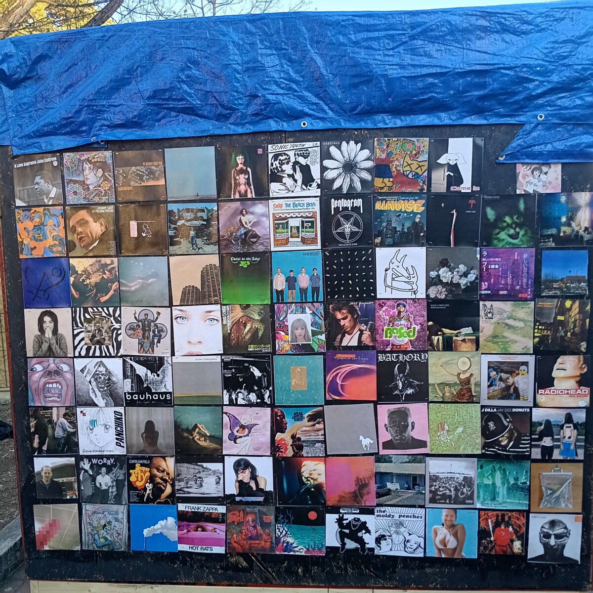 A wall of a plywood shack covered in various album covers.