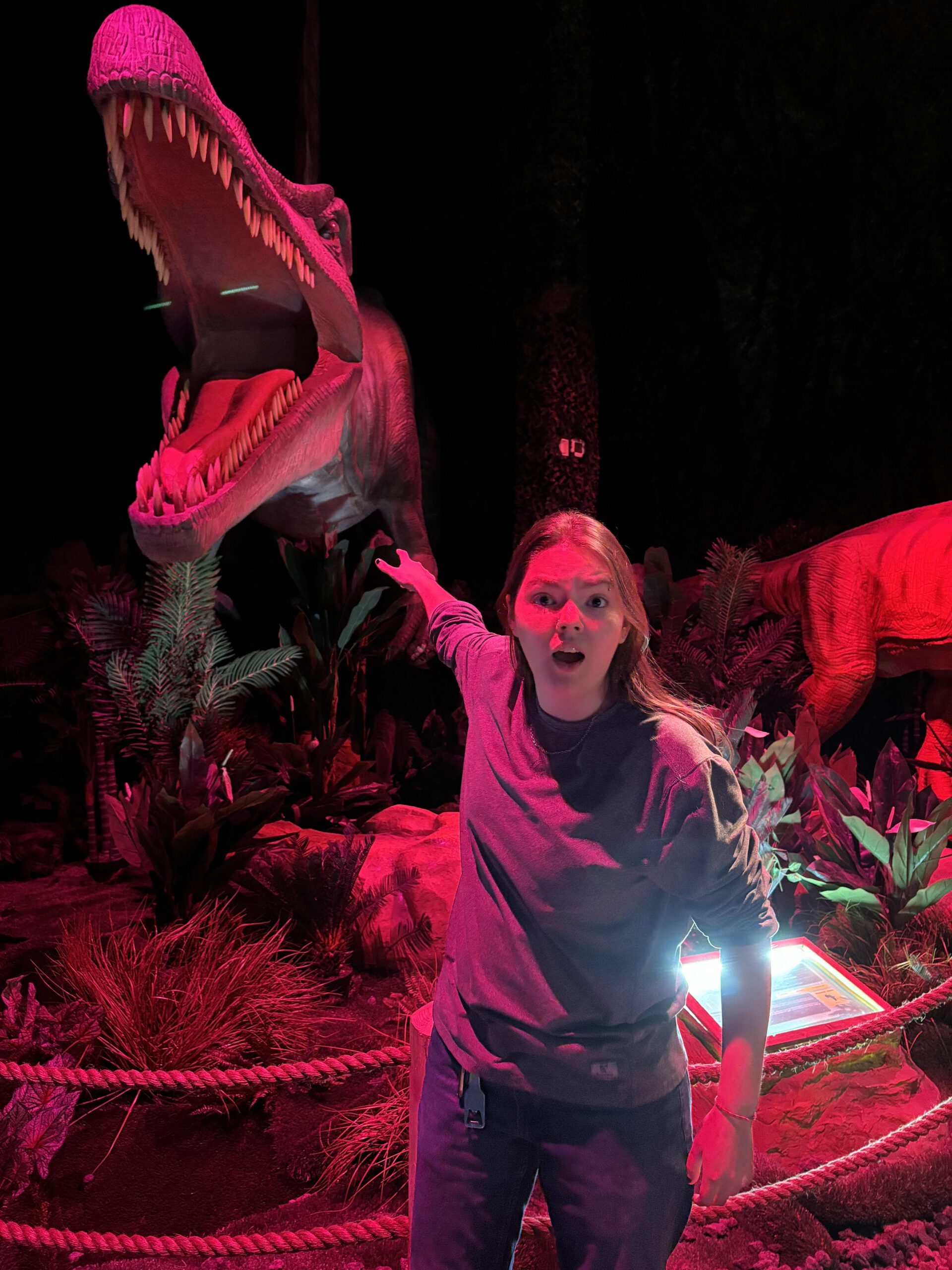 Sarah Scrimble pointing backward toward a fierce T-rex with his mouth open.