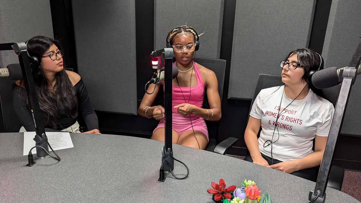 Three women sit in front of microphones in a radio studio.