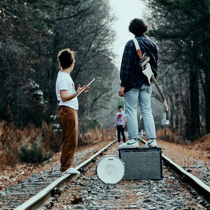 The band Stan Y Denghy standing on railroad tracks with musical equipment, surrounded by trees.