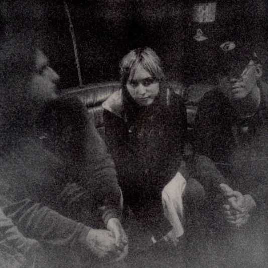 Members of the band applefield sitting on a couch in a dimly lit, grainy black-and-white photograph.