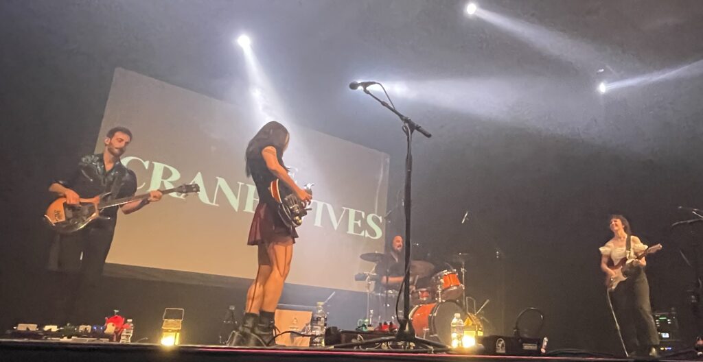 A wide shot of The Crane Wives performing. Emilee Petersmark and Kate Pillsbury are facing each other with their instruments.