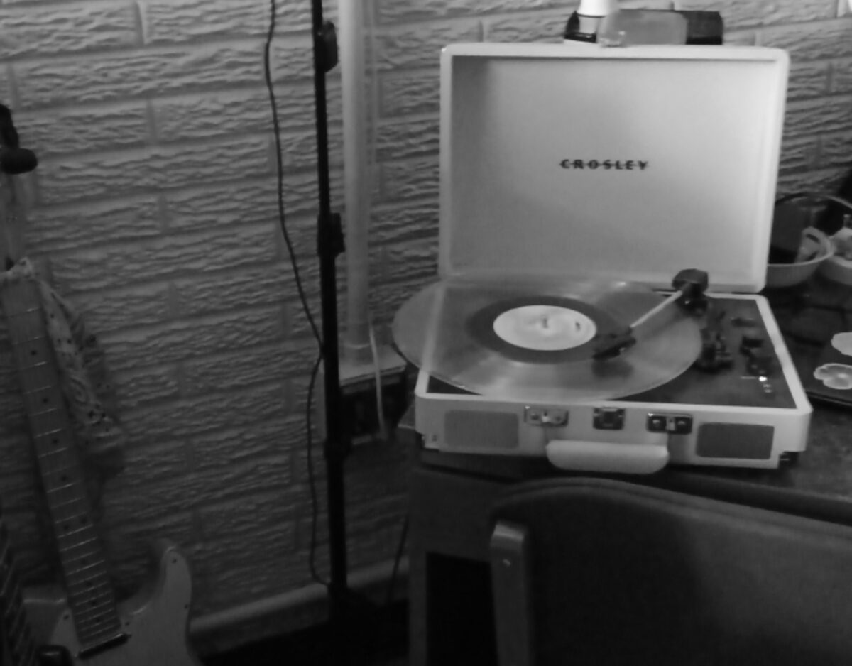 Black and White photo of record player on desk with guitar in corner