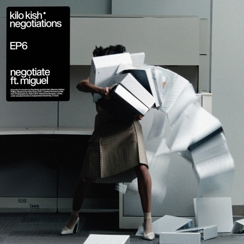 Kilo Kish in the center of the image, holding a tall stack of binders and papers that are falling on her.