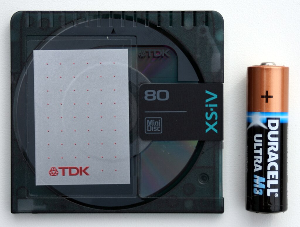 A black minidisc next to a AA battery