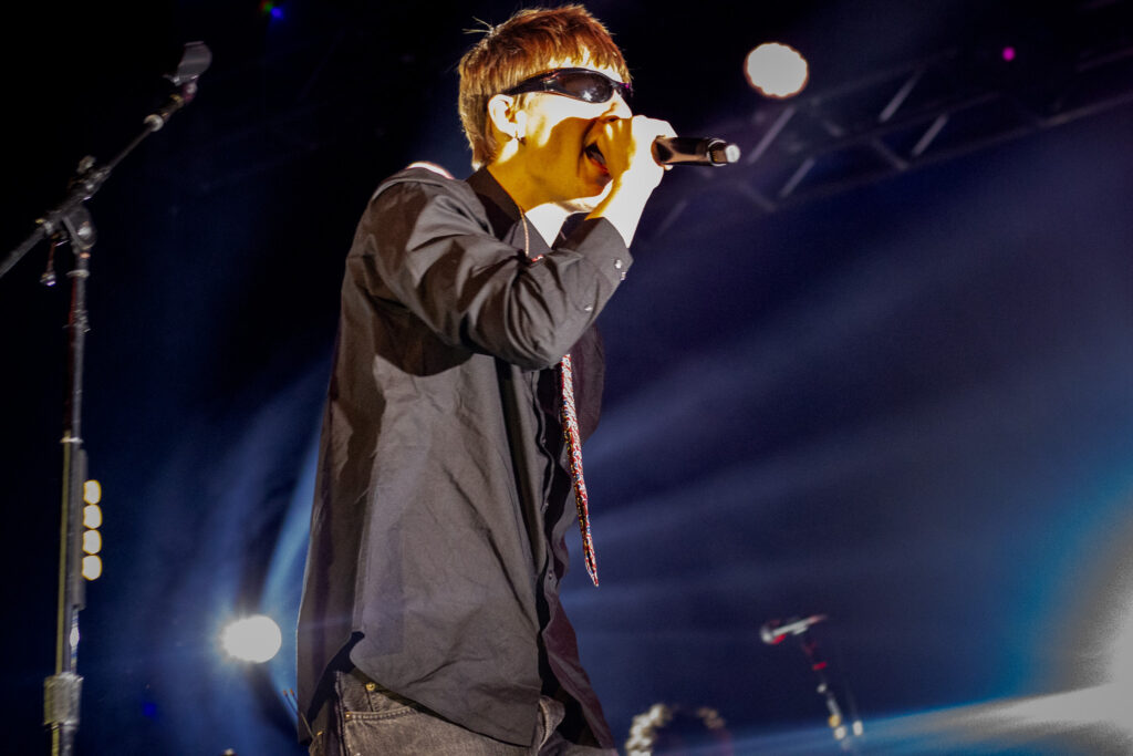 Malcolm Todd is brightly lit up by lights behind him while singing into a microphone.