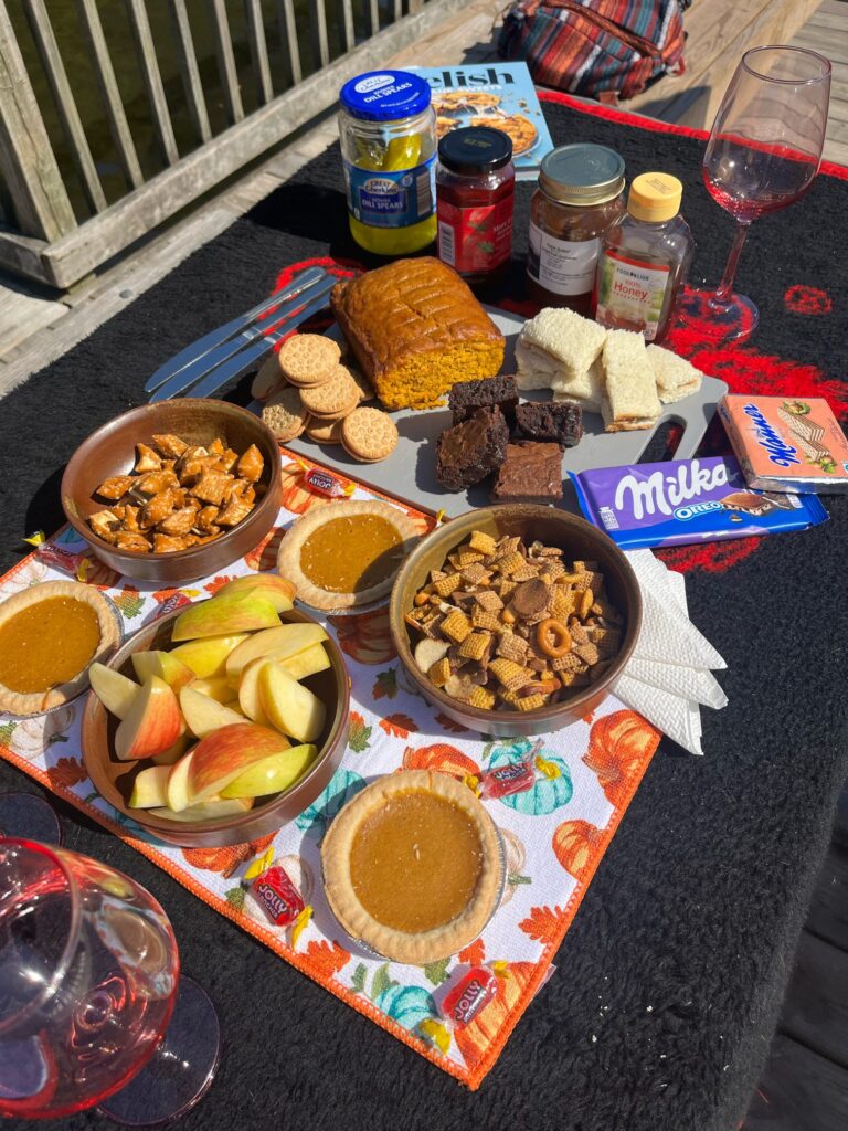 An outdoor picnic table with a fall spread of foods (mini pumpkin pies, apple slices, pumpkin bread, finger sandwiches, etc.)