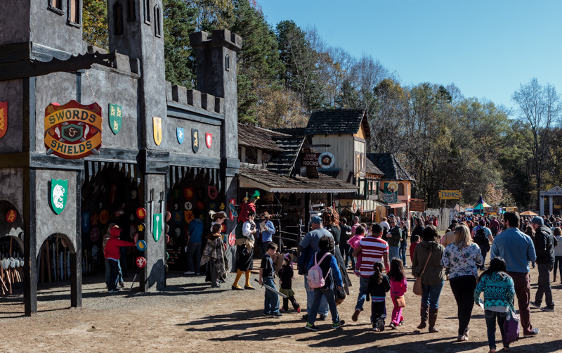 People standing in front of an old timey castle-like shop for wooden shields and swords