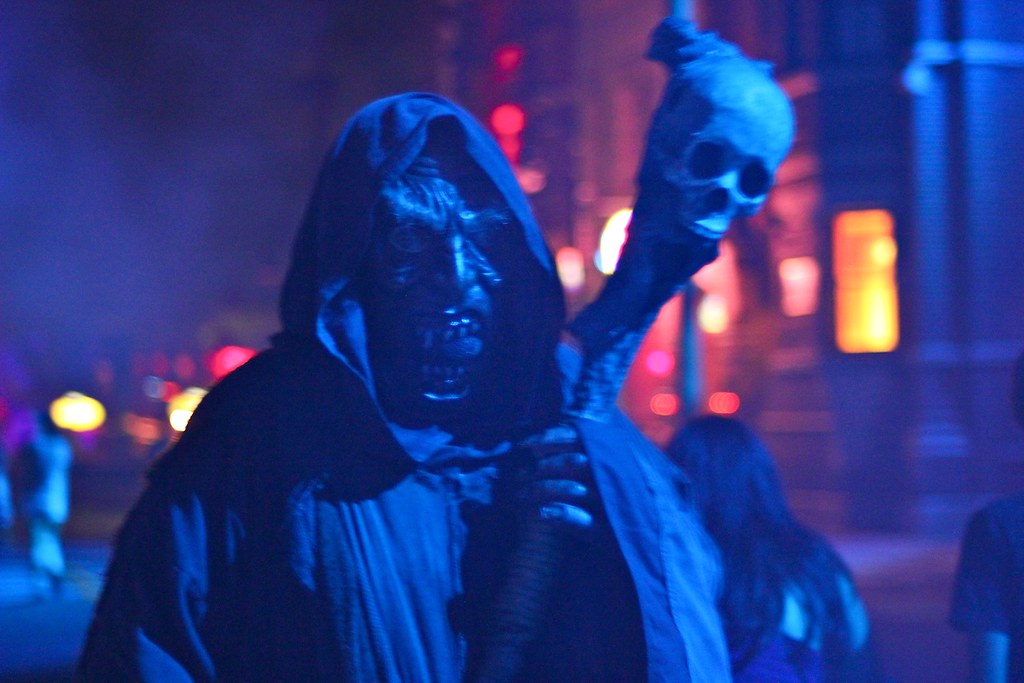 Scare actor in a cloak and scary mask holding a staff with a skull in dim lighting