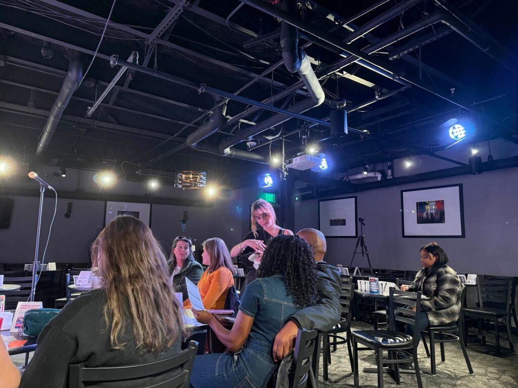 A intimate seated venue of guests at Sureni Weerasekera's comedy show, illuminated by yellow and blue stage lights. Photo by Killian Le, taken with Permission.