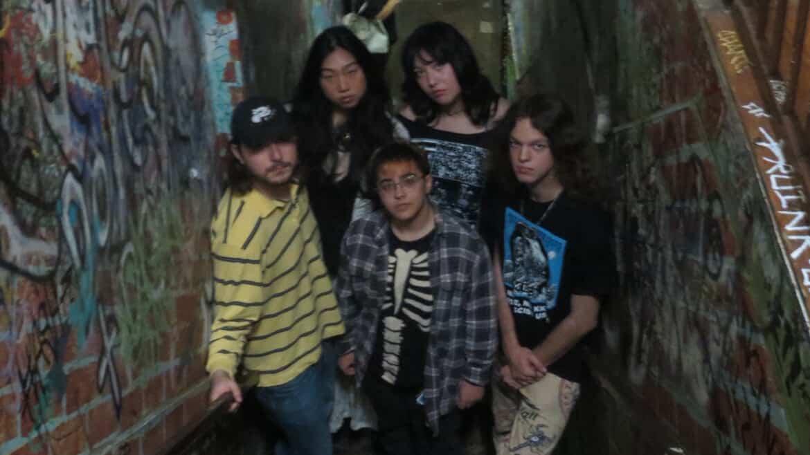 Five young adults posed together in a graffitied brick alley