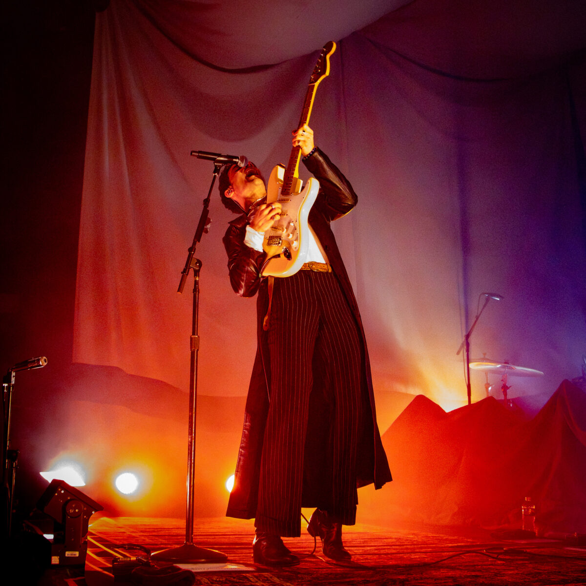 Del Water Gap singing into microphone while leaning back and playing electric guitar