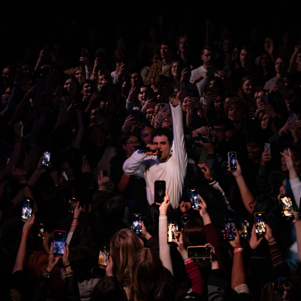 Del Water Gap in the middle of the crowd with one hand up singing and jumping.