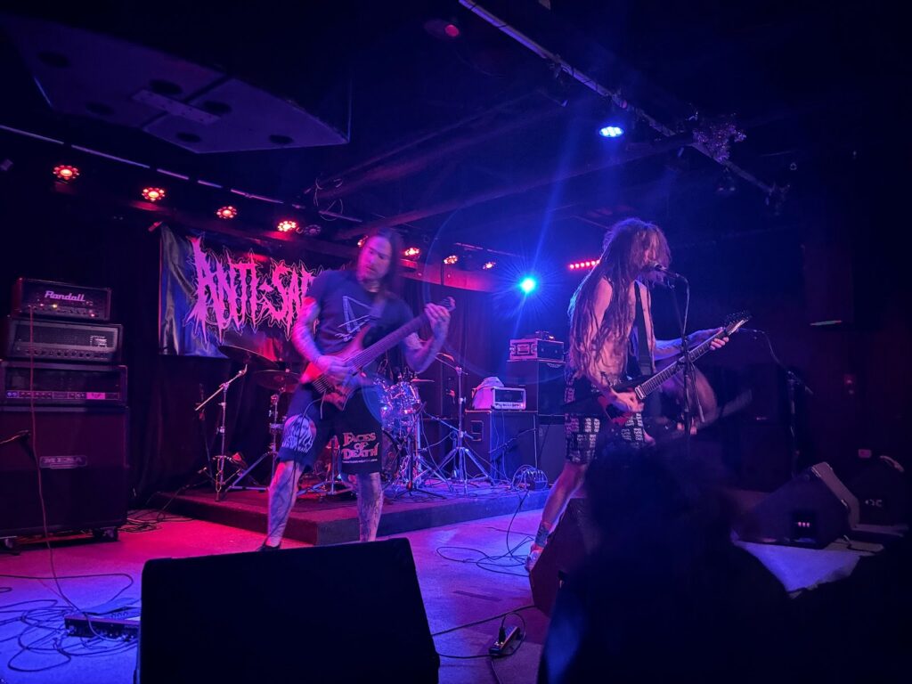 A blue-lit stage with members of Noctomb playing guitars. The lead guitarist and bass guitarist are mainly featured. By Killian Le, used by permission.