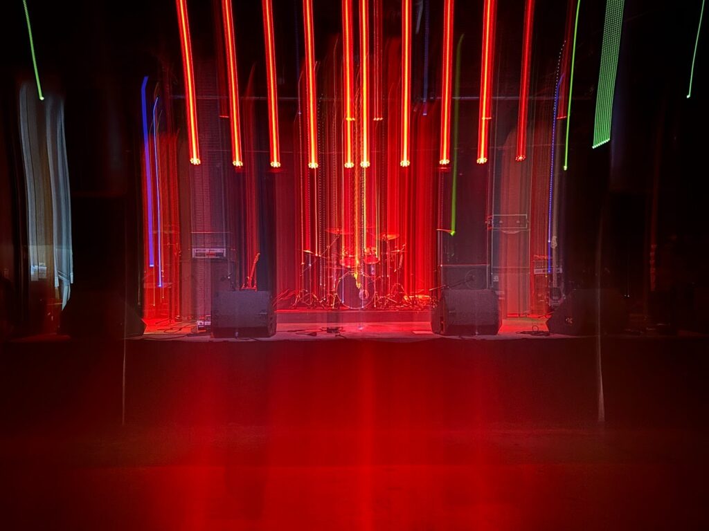 An atmospheric red light smeared front view of the Chapel of Bones stage. By Killian Le, used by permission.