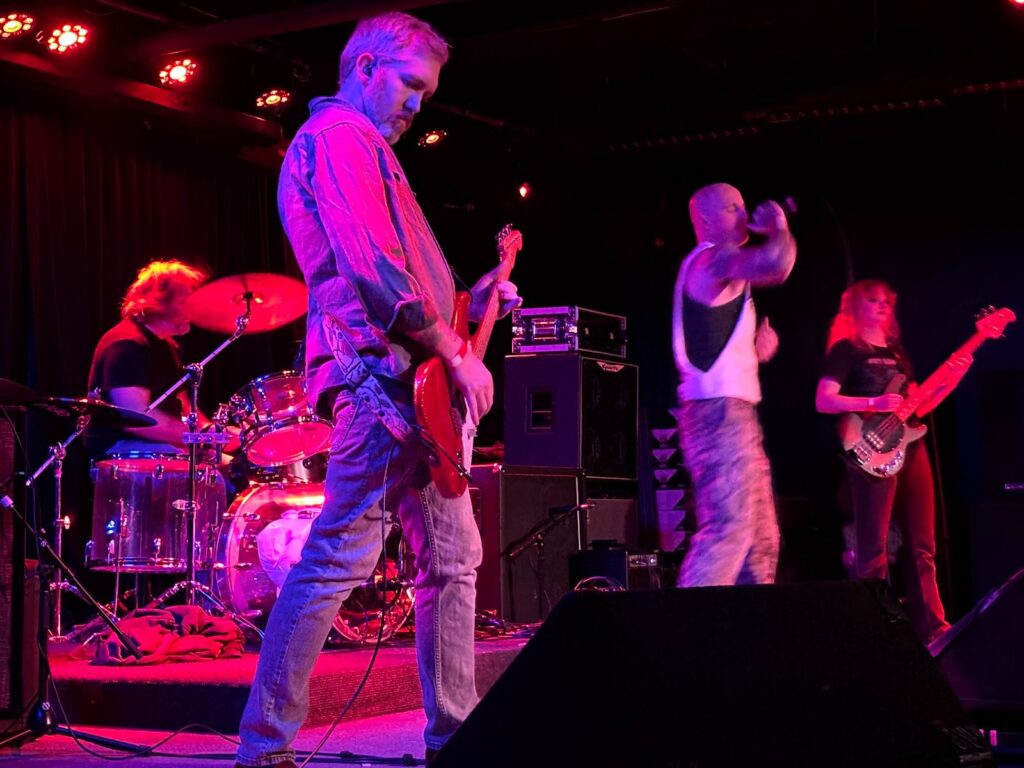 All four members of Dunmharu, pink-red lit by stage lights. By Killian Le, used by permission.