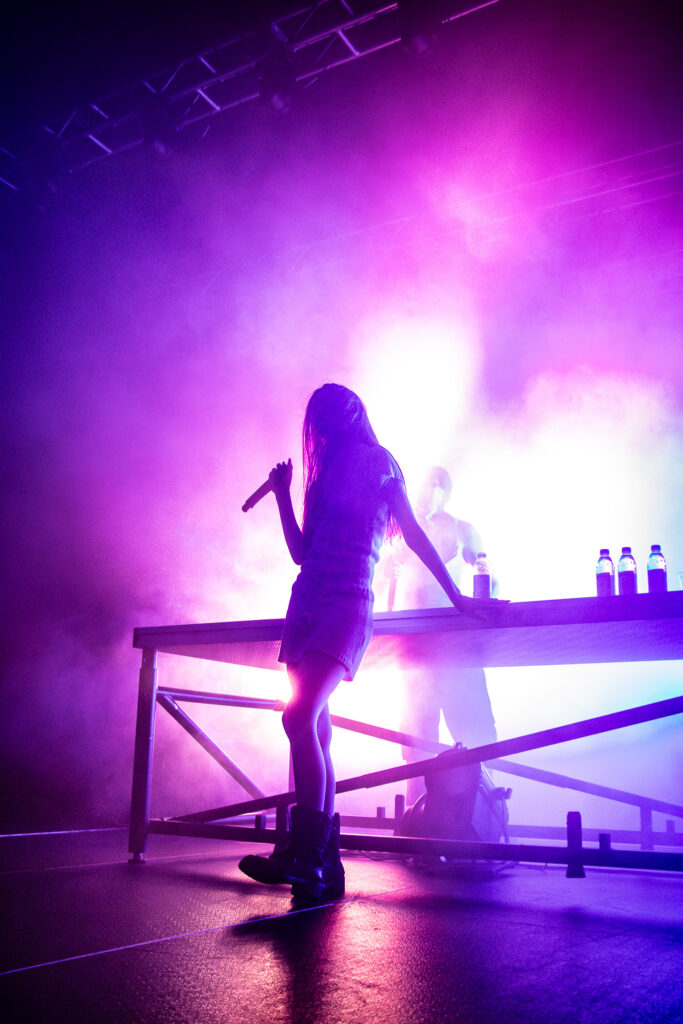 Snow Strippers on stage at DJ table with pink and purple lights behind.