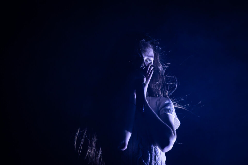 Snow Strippers' Tatiana Schwainger singing into microphone and half lit by blue stage lights.