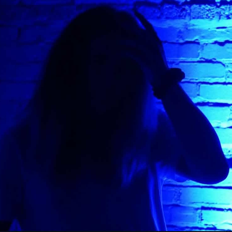 Silhouette of a person against a bright blue-lit brick wall.