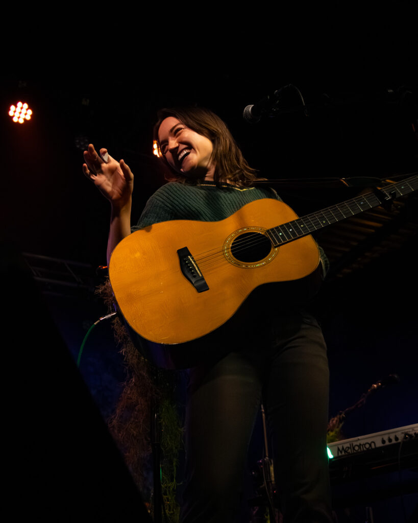Annika Bennett laughing to the side with acoustic guitar.