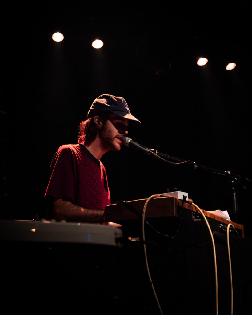 John Andrews sitting at a keyboard while singing into a microphone.