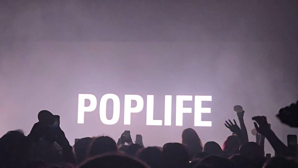 "Poplife" is on the screen of the stage, in front of a crowd of hands.