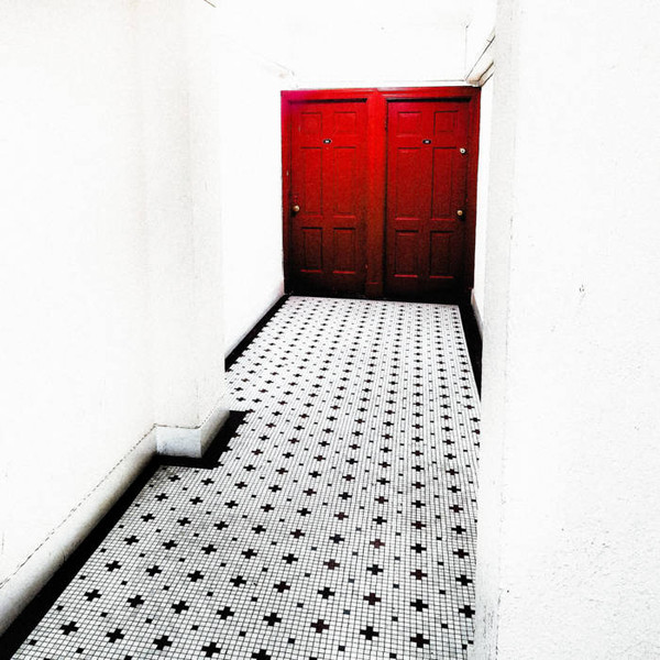 Album cover showing a black and white tile floor with black crosses going down a long white hallway ending at double red doors.
